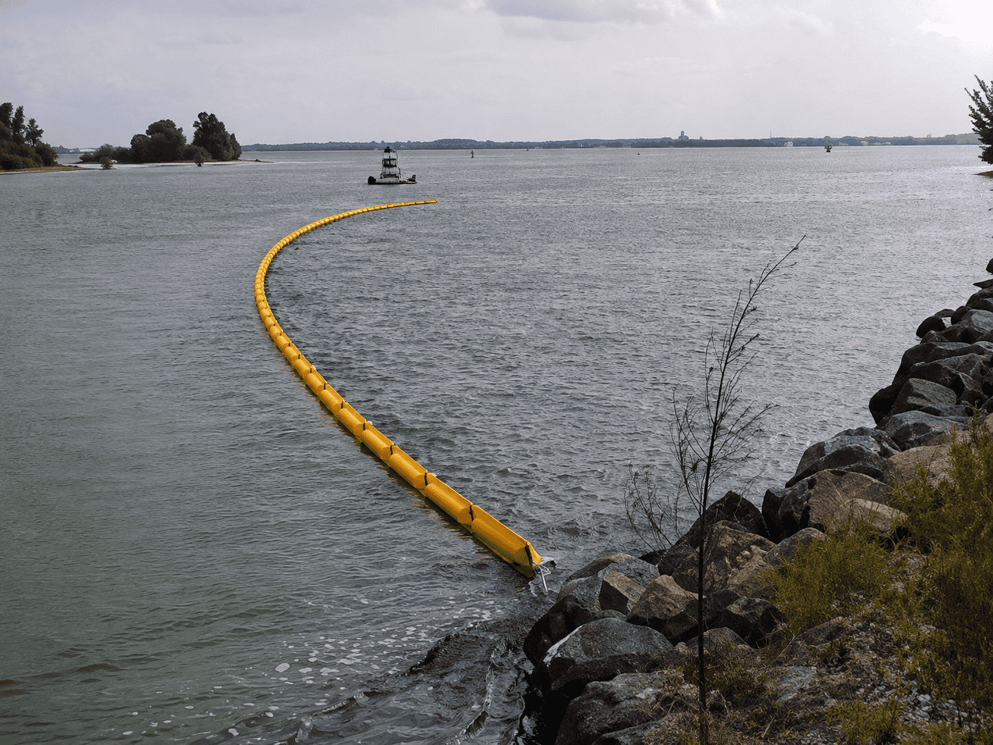 Containment Boom – Fast Current – Protected Water – Enviro-USA Yellow standard containment boom deployed across a waterway near a rocky shoreline for oil spill and floating pollutant containment.