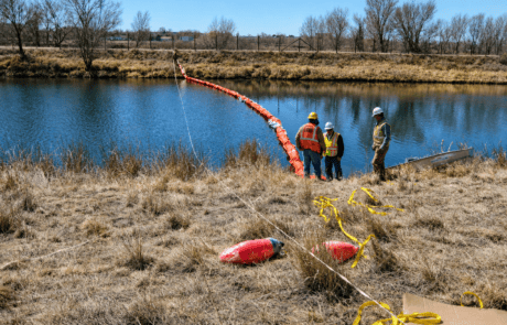Oil Containment Boom Deployment for Spill Response Orange oil containment boom being deployed across a waterway by environmental response crews to help control oil and floating pollutants.