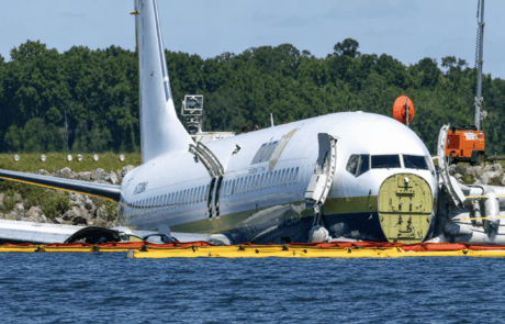 Oil Containment Boom for Emergency Fuel Spill Response Yellow and orange oil containment boom deployed around a damaged aircraft near water to help contain fuel, oil, and other floating hydrocarbons during emergency spill response.