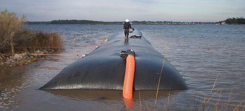 Geotextile Dewatering Tube for Dredging and Sediment Management Large geotextile dewatering tube installed along a shoreline to contain dredged sediment and filter water during dewatering operations.